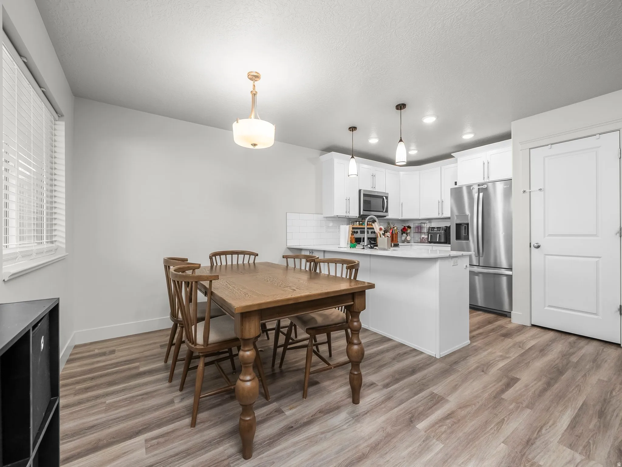 Open-concept kitchen and dining area featuring light wood-finish flooring, white cabinetry, stainless steel appliances, and a tile backsplash