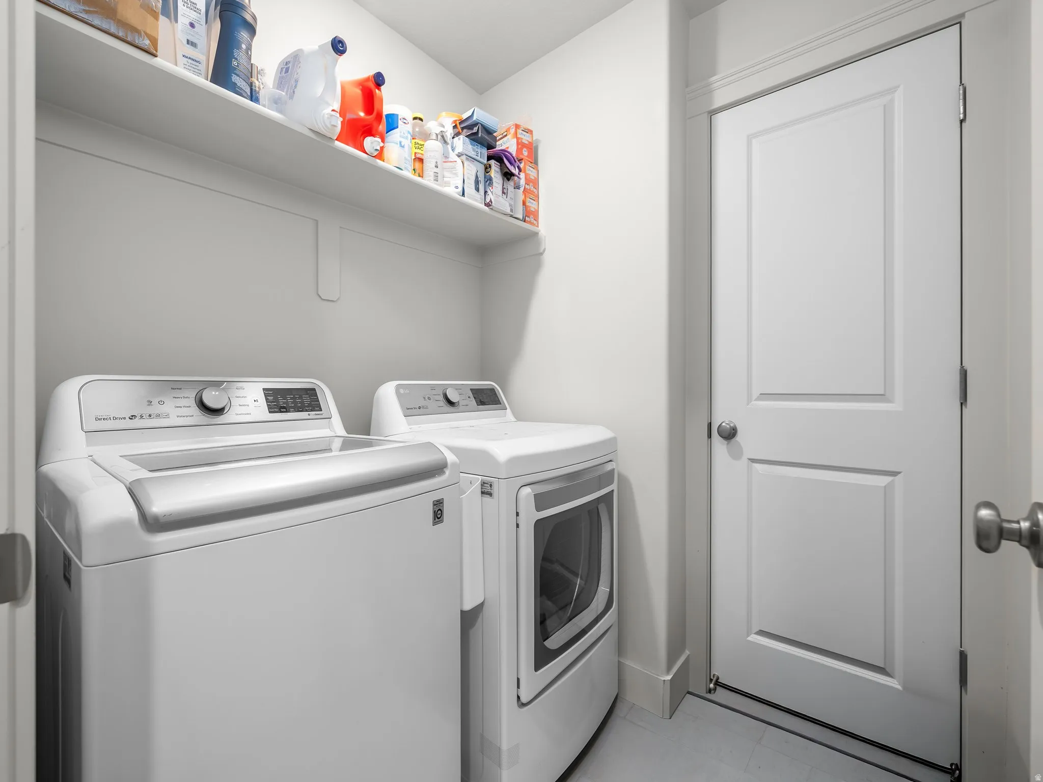 Laundry area featuring a built-in shelf, two permanent appliance hookups, a paneled interior door with a round knob, and light-toned flooring