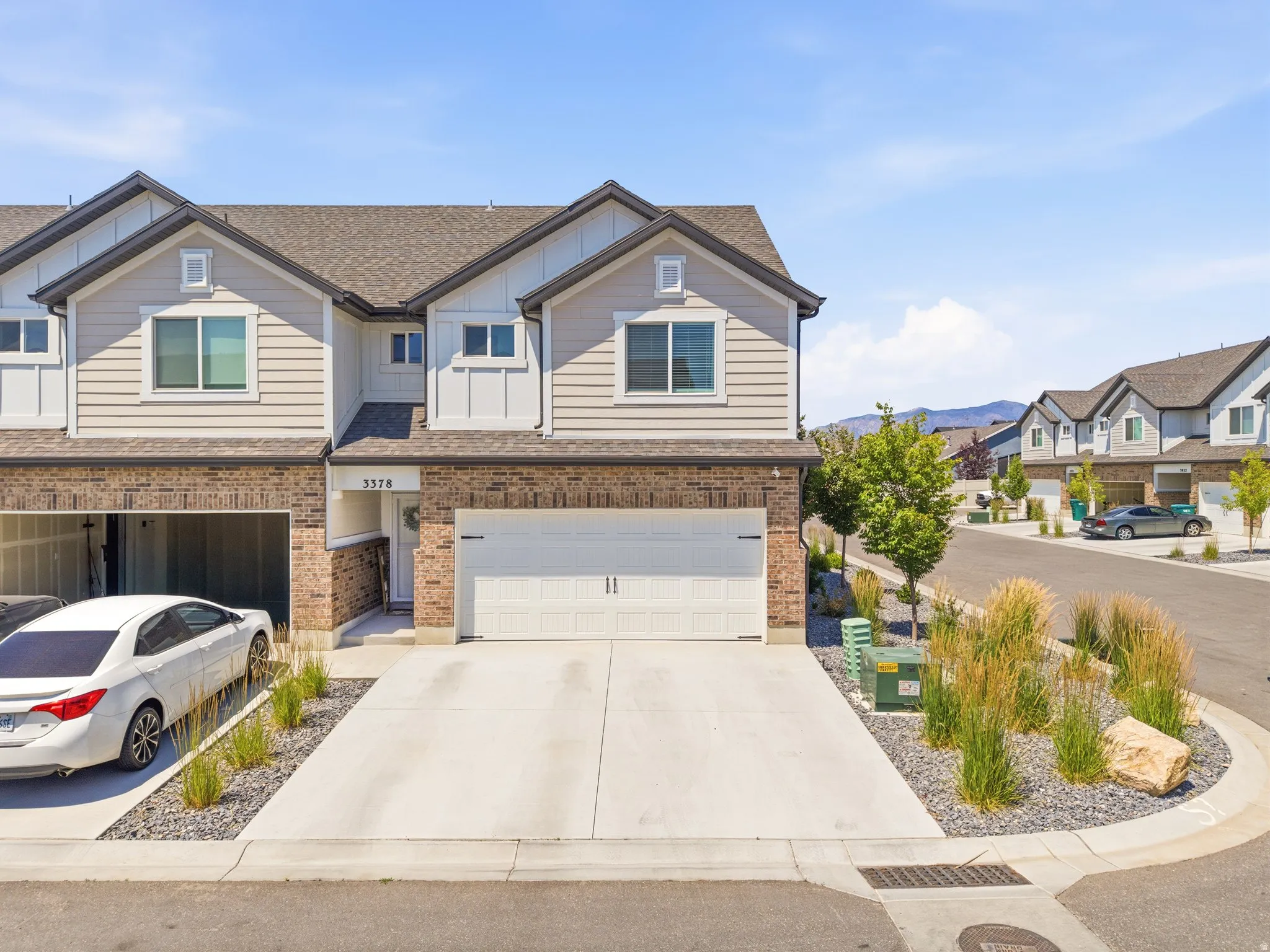Contemporary townhome featuring a two-car garage, brick facade, light-toned siding, and a concrete driveway