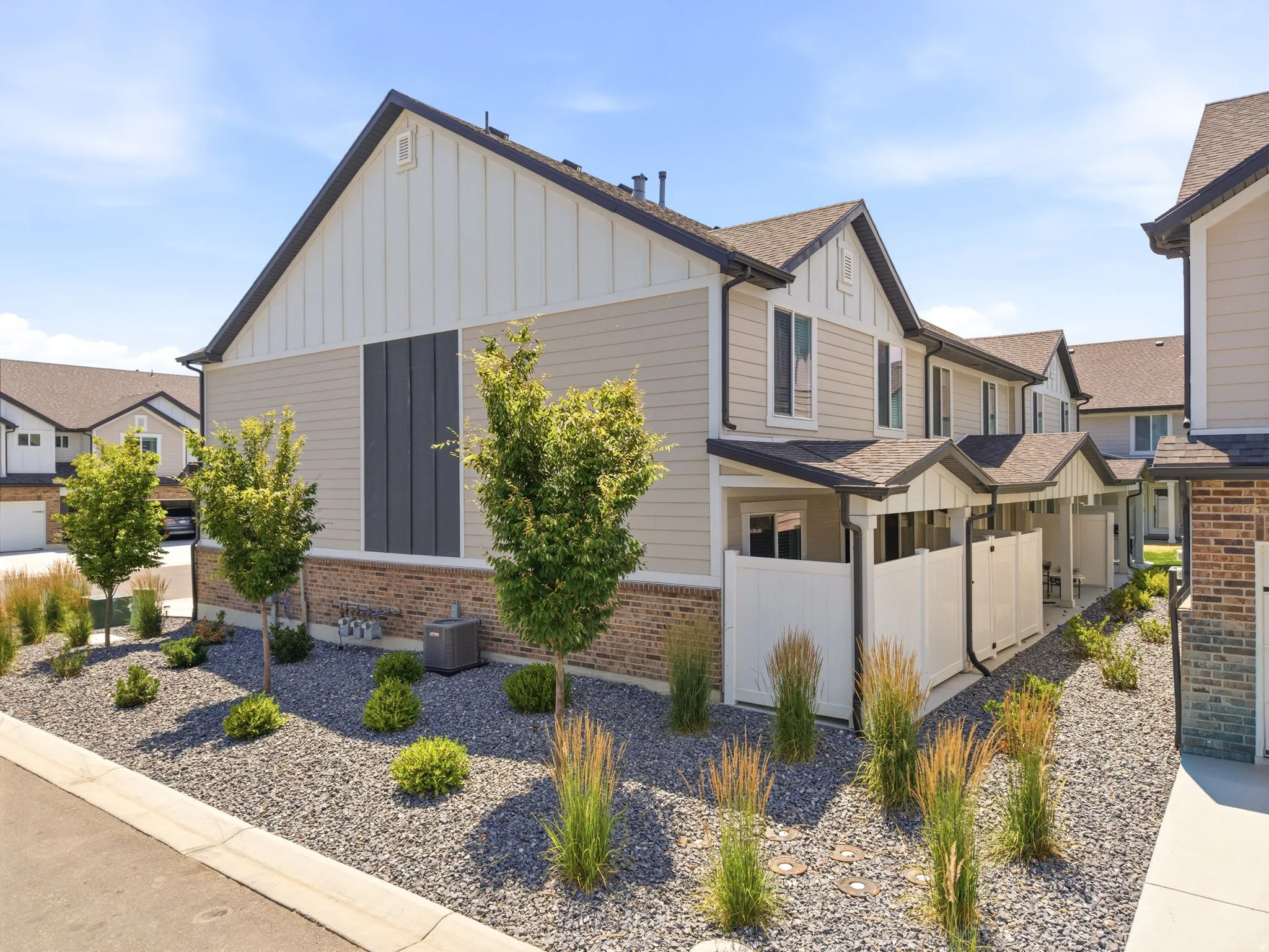 Townhome exterior featuring tan siding, dark brown roofing, and a white gable accent