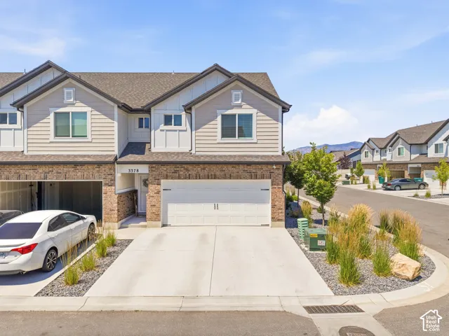 Contemporary townhome featuring a two-car garage, brick facade, light-toned siding, and a concrete driveway
