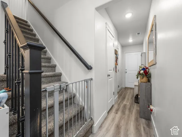 Carpeted staircase with dark wood newel post and balusters, featuring a light wood-finish flooring hallway with white walls, recessed lighting, and white paneled doors