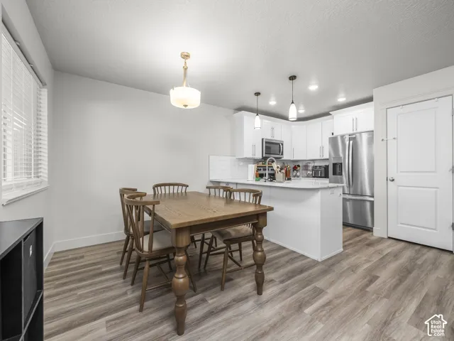 Open-concept kitchen and dining area featuring light wood-finish flooring, white cabinetry, stainless steel appliances, and a tile backsplash