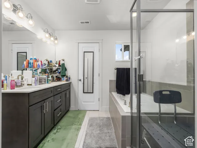 Bathroom featuring a dual vanity with dark wood-finish cabinetry, a large frameless mirror, a built-in soaking tub with tiled surround, and a glass-enclosed shower