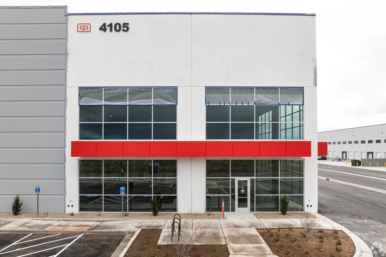 Modern industrial building featuring a white facade with red accents, expansive glass storefronts, and a visible building number