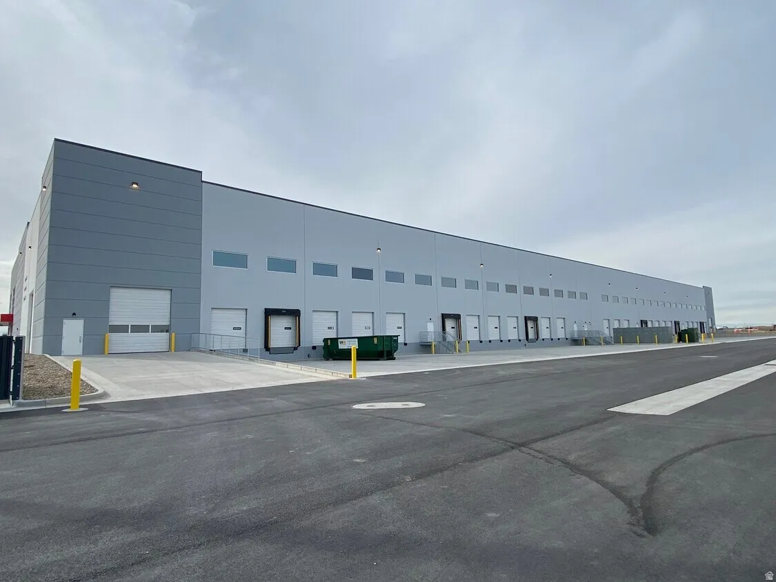 Expansive industrial building featuring multiple loading docks, roll-up doors, an asphalt parking lot, and a modern grey exterior