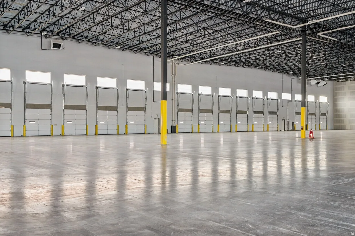 Expansive interior space featuring a polished concrete floor, high exposed truss ceiling, and multiple overhead doors with transom windows