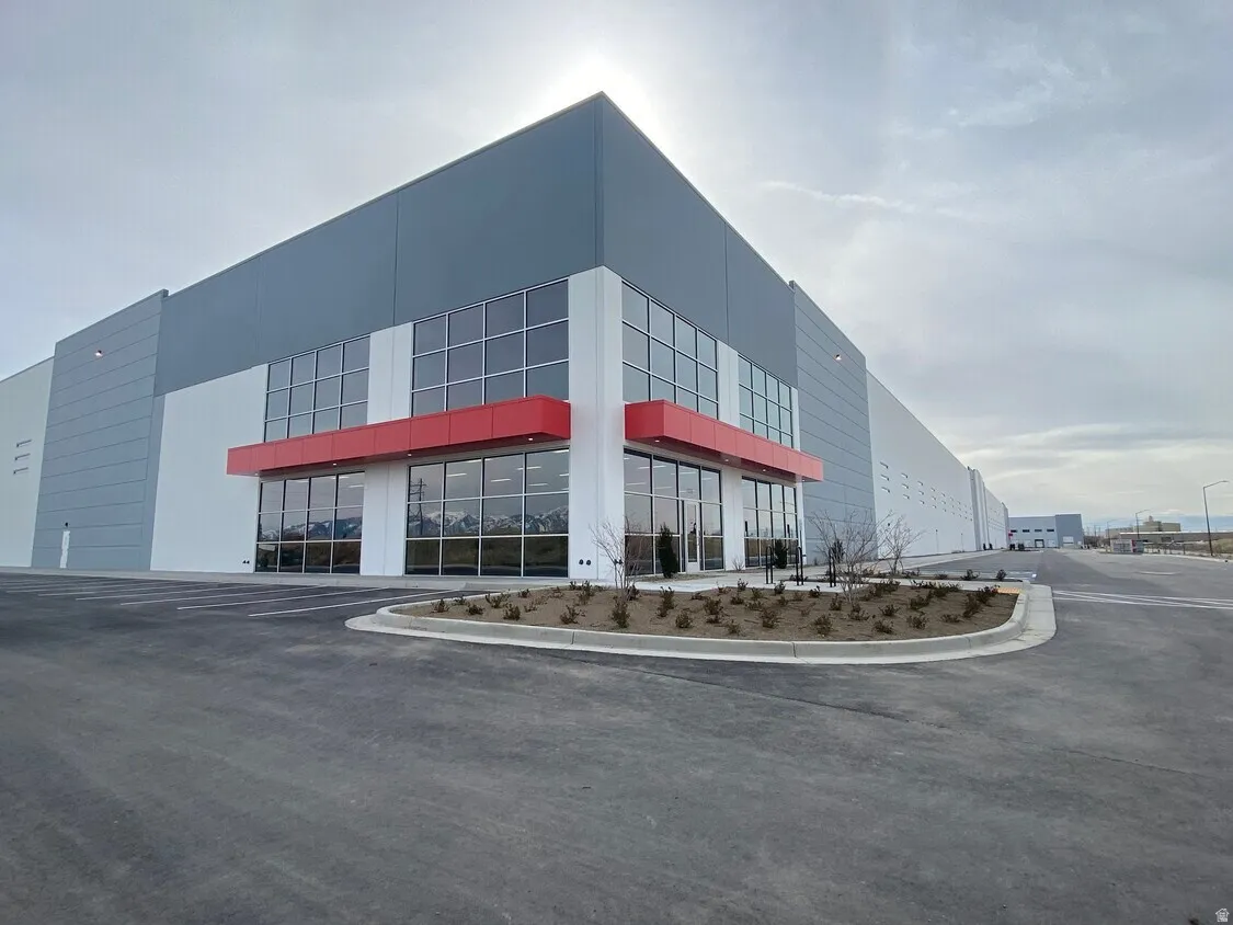 Modern commercial building featuring extensive glass curtain walls, a distinctive red architectural overhang, and a clean gray and white exterior