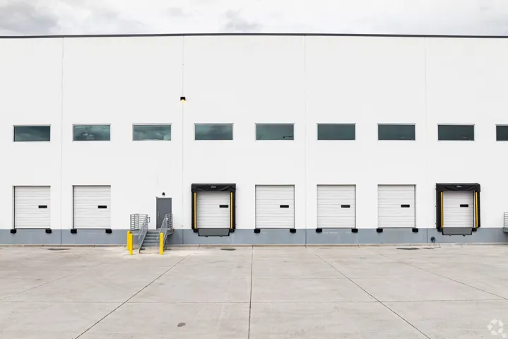 Industrial building exterior featuring a white facade, multiple dock-high doors, upper-level windows, and a concrete loading area