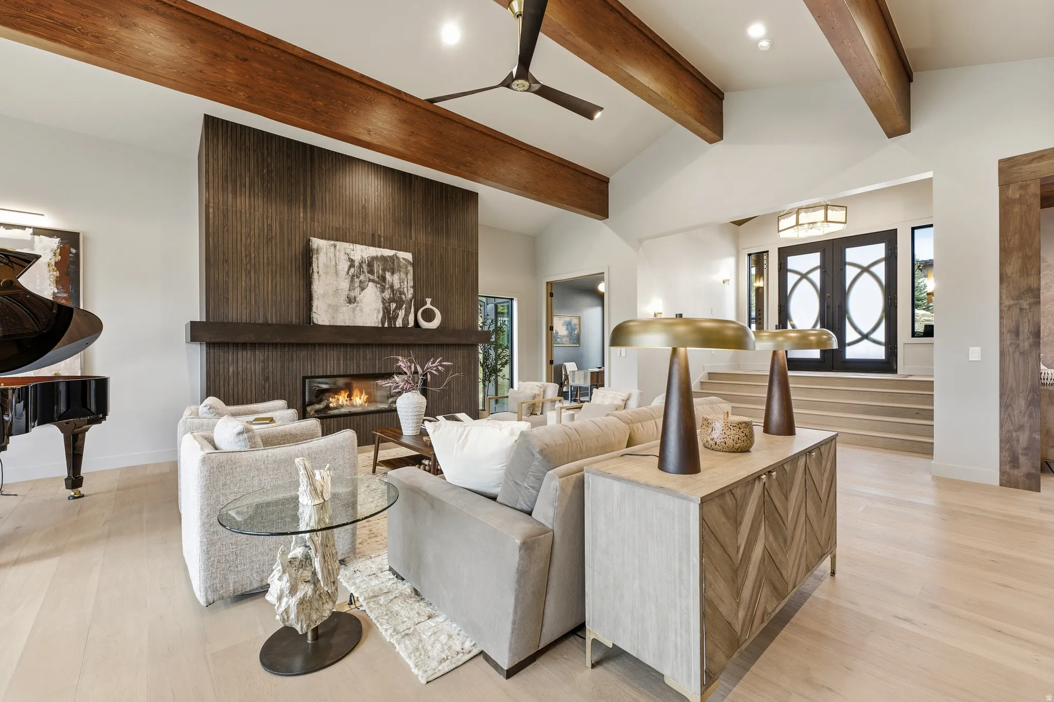 Vaulted ceilings with exposed wood beams, a linear fireplace with a textured dark wood surround, and light wood-finish flooring