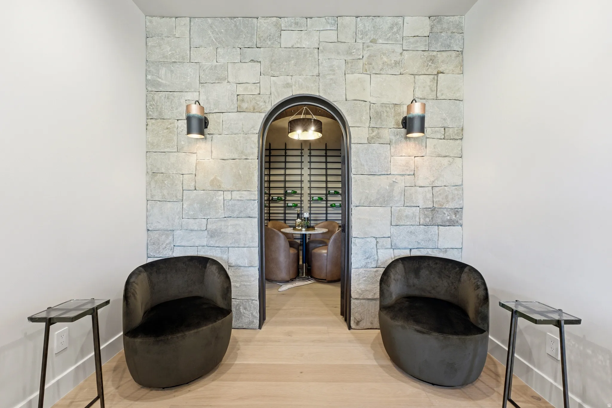 Stone accent wall with an arched doorway, light wood-finish flooring, and wall-mounted sconce lighting