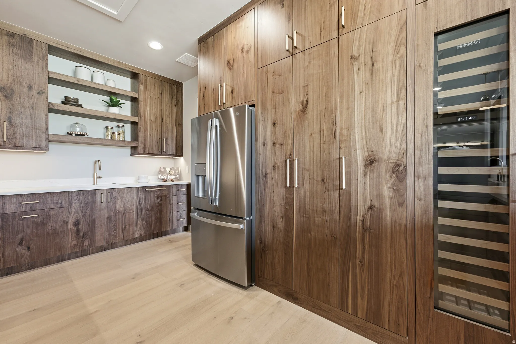 Custom wood-finish cabinetry with integrated stainless steel refrigerator, separate wine refrigeration, white countertops, and wood-finish flooring