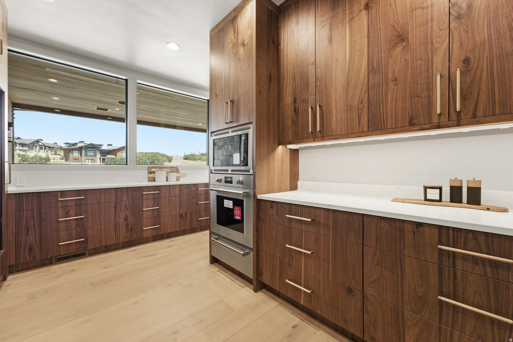 Custom wood cabinetry with integrated stainless steel appliances, light wood-finish flooring, and white countertops