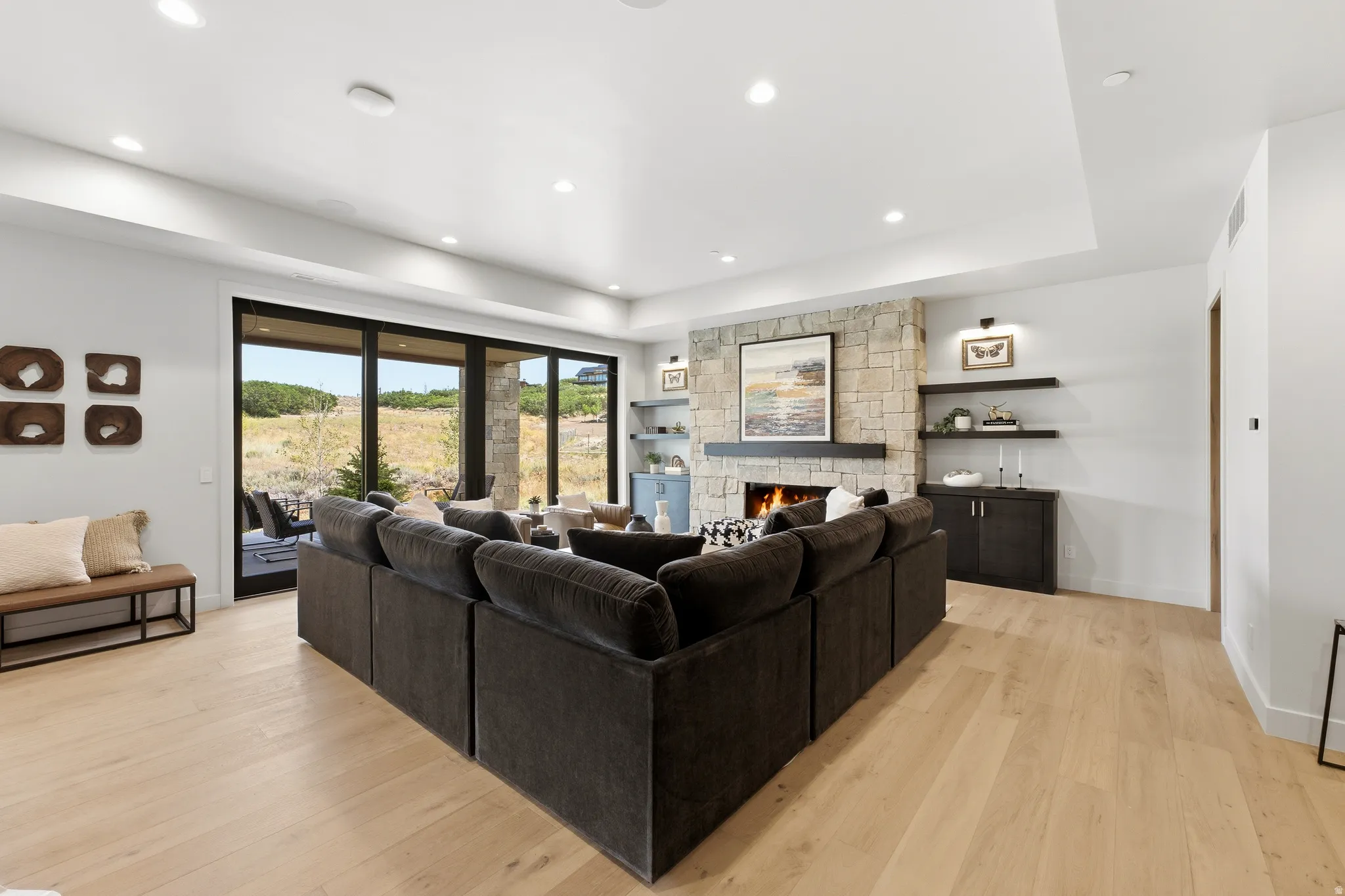 Expansive living area featuring light wood-finish flooring, a stone-clad fireplace, and recessed lighting