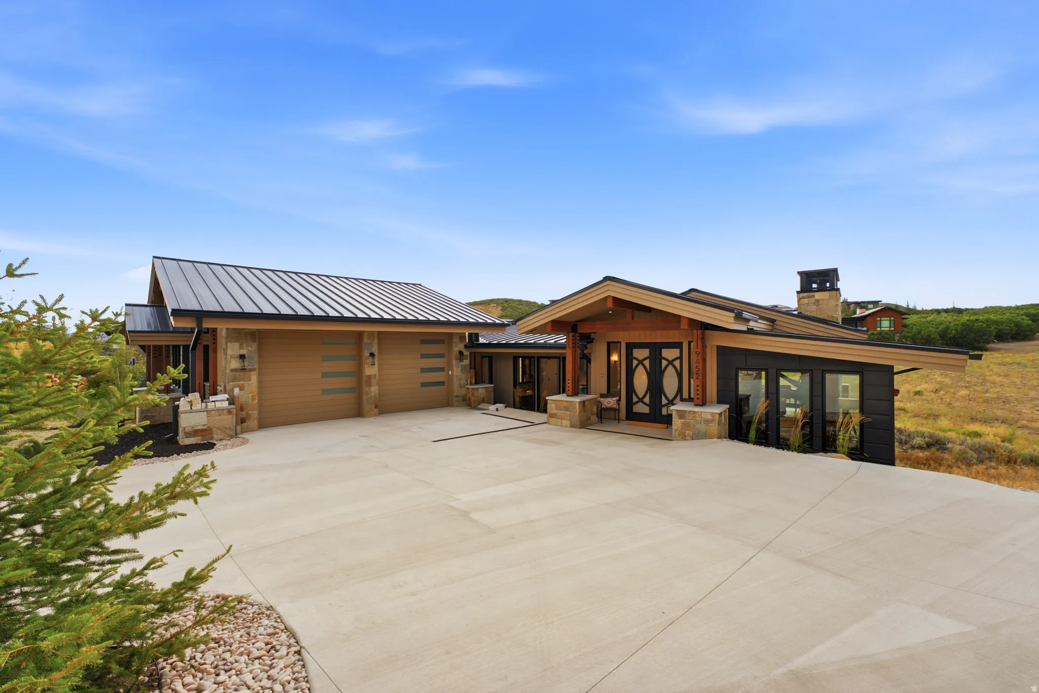 Contemporary exterior with a metal roof, stone and wood-paneled accents, and a wide concrete driveway