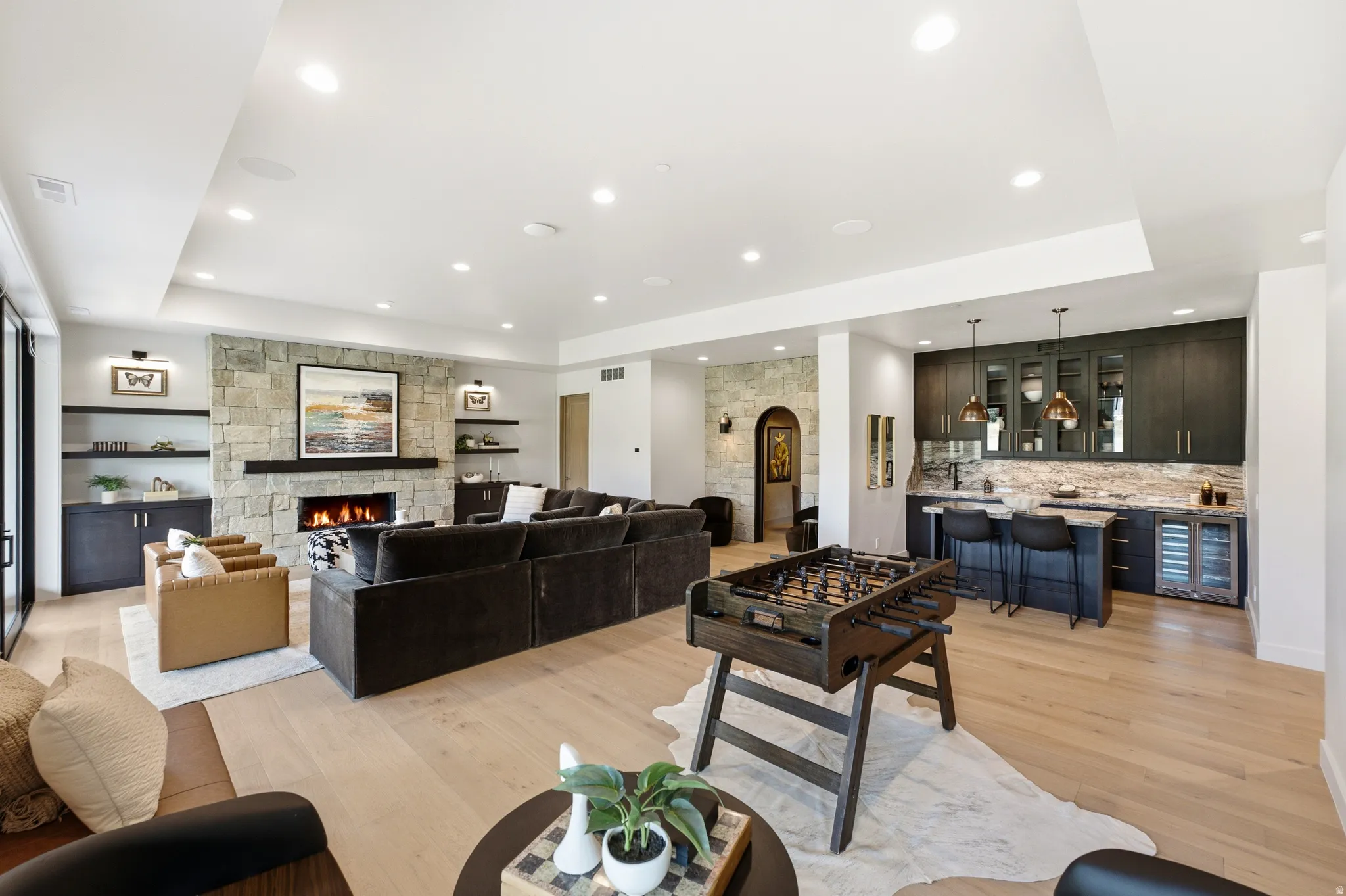 Spacious living area featuring light wood-finish flooring, a stone-clad fireplace with a dark mantel, and built-in shelving