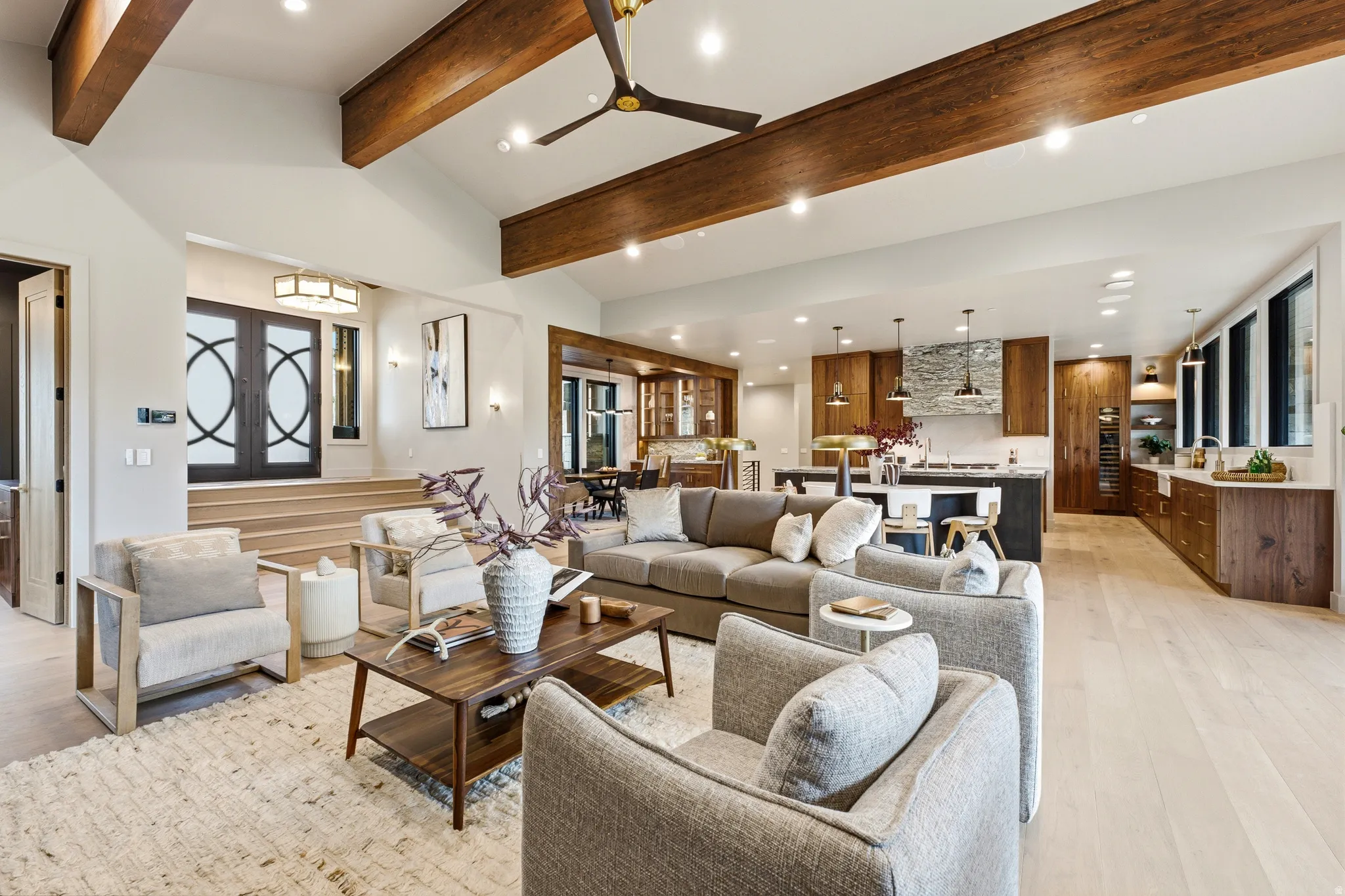 Vaulted ceiling with exposed wood beams, light wood-finish flooring, recessed lighting, and a modern kitchen with wood cabinetry