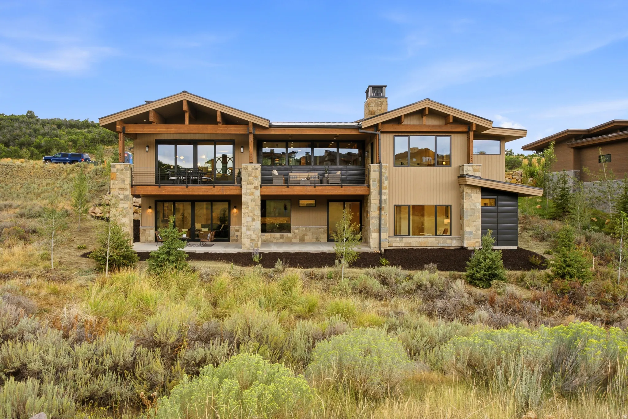 Contemporary multi-level residence featuring a stone and siding exterior, expansive upper-level balcony, lower-level patio, and large windows