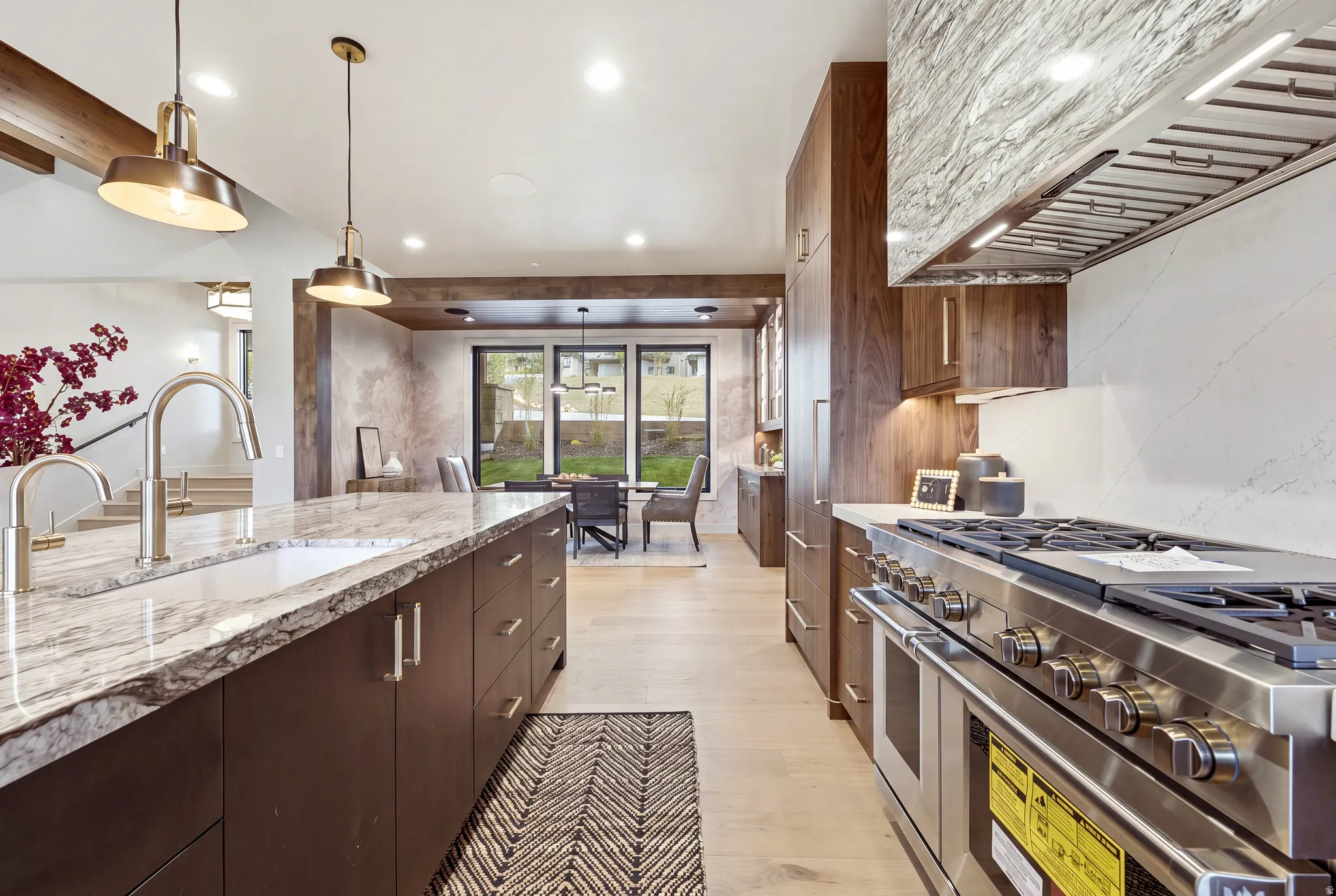 Gourmet kitchen with a large central island, stainless steel range with overhead hood, wood-finish cabinetry, and light wood-finish flooring