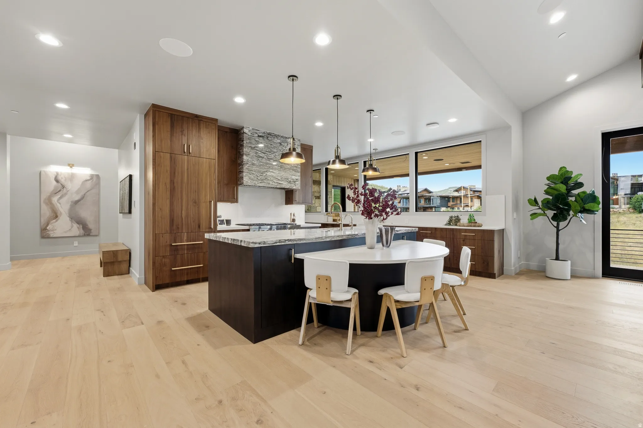 Wide plank wood-finish flooring, recessed lighting, expansive windows, dark wood-finish cabinetry, and a stone-clad range hood
