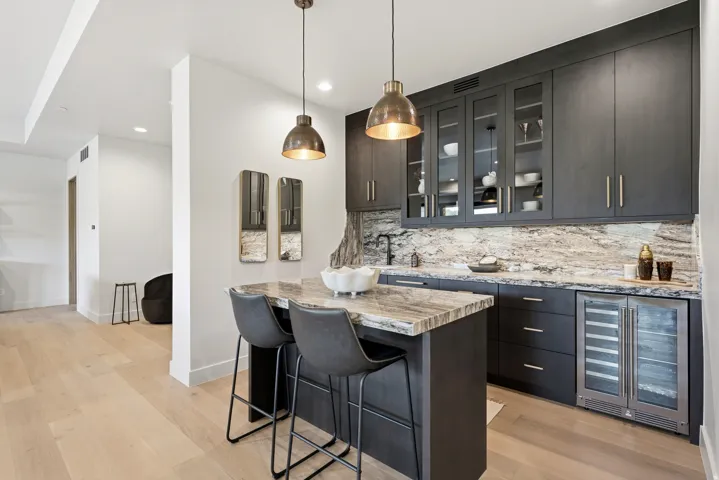 Contemporary wet bar featuring dark wood cabinetry, integrated beverage refrigerator, stone countertops, and coordinated backsplash