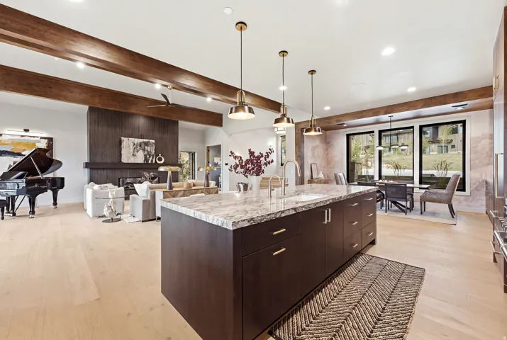 Kitchen island with a light-toned countertop and integrated sink, recessed lighting, wood-finish flooring, and exposed ceiling beams