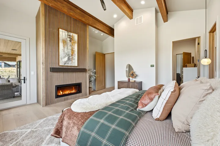 Vaulted ceilings with exposed wood beams, a vertical slat wood accent wall, an integrated electric fireplace, light wood-finish flooring, and a glass-paned door