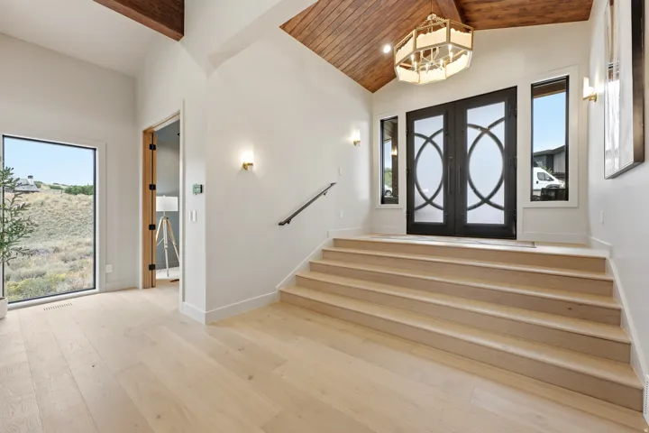 Vaulted wood-finish ceiling with exposed beams, wood-finish flooring, custom double entry doors with decorative glass panels, and built-in wall sconces