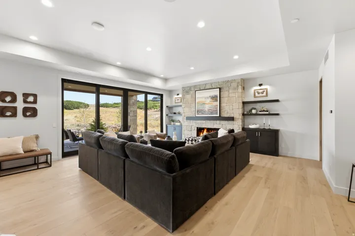 Expansive living area featuring light wood-finish flooring, a stone-clad fireplace, and recessed lighting