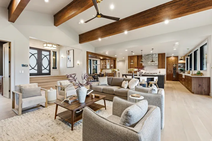 Vaulted ceiling with exposed wood beams, light wood-finish flooring, recessed lighting, and a modern kitchen with wood cabinetry
