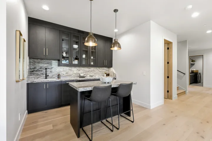 Built-in wet bar featuring dark cabinetry, stone countertops, integrated sink with matte black faucet, and glass-front upper cabinets
