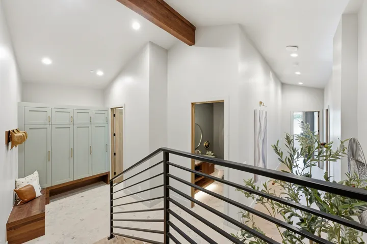 Vaulted ceilings with exposed wood beam, recessed lighting, built-in cabinetry with bench, and a contemporary metal staircase railing