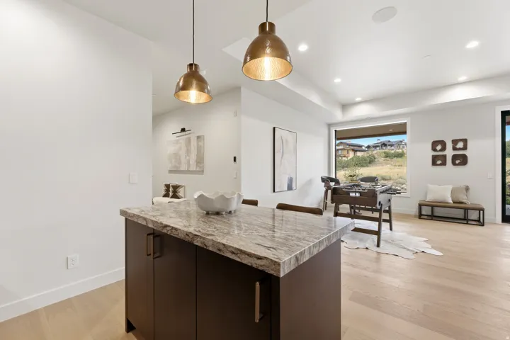 Kitchen island with a light-toned stone countertop, bronze pendant lighting, wood-finish flooring, and a large window