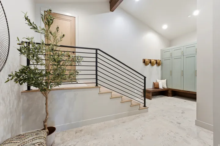 Light-toned flooring, staircase with a black metal railing, built-in mudroom storage, and a light wood-finish door