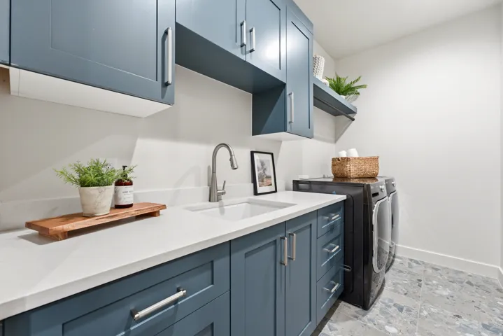 Blue cabinetry with brushed nickel hardware, white countertop, integrated sink with gooseneck faucet, and patterned tile flooring