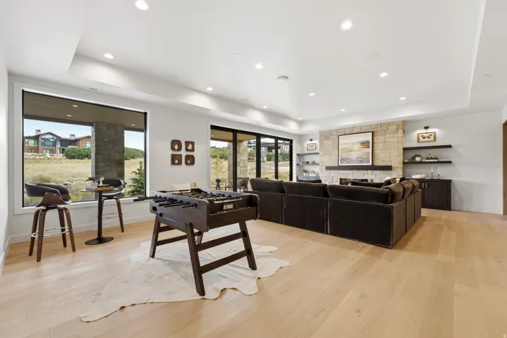 Spacious room featuring light wood-finish flooring, a stone-clad fireplace with a dark wood mantel, recessed lighting, and large windows