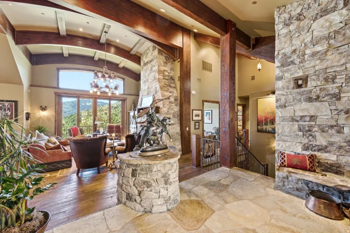 Expansive interior featuring high vaulted ceilings with exposed wood beams, a stone accent wall, wood-finish flooring, and large glass doors opening to the exterior