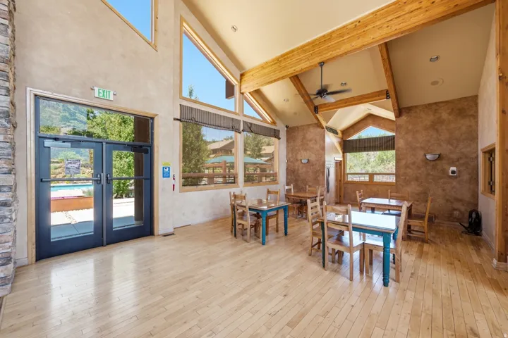 Spacious common area featuring vaulted ceilings with exposed wood beams, light wood-finish flooring, and large windows