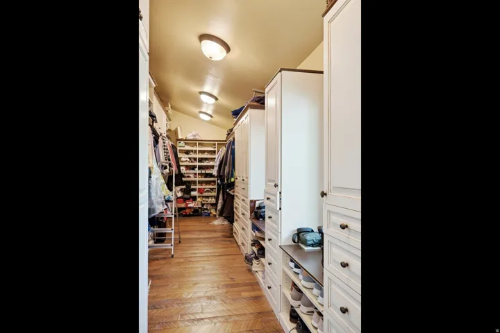 Custom closet system featuring wood-finish flooring, recessed lighting, built-in shelving, drawers, and cabinet storage