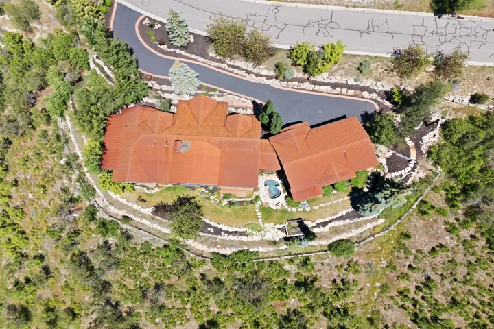 Terracotta-tiled roof property featuring a private driveway, terraced landscaping with stone retaining walls, a built-in swimming pool, and surrounding natural foliage