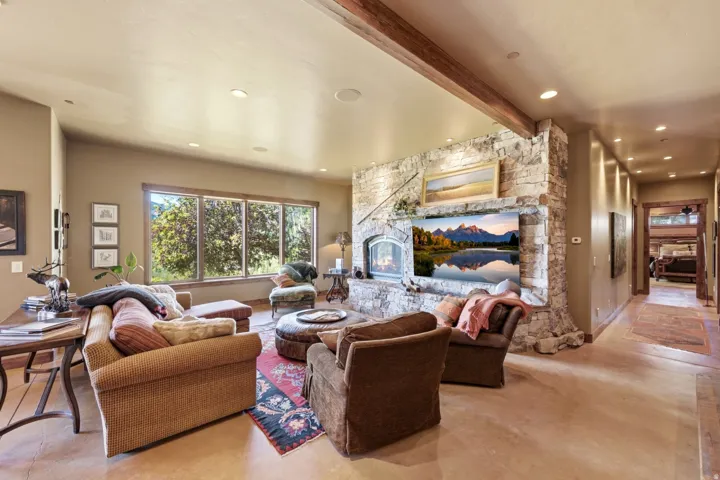 Spacious living area featuring a stone-clad fireplace and hearth, a large picture window, exposed wood beams, and recessed lighting