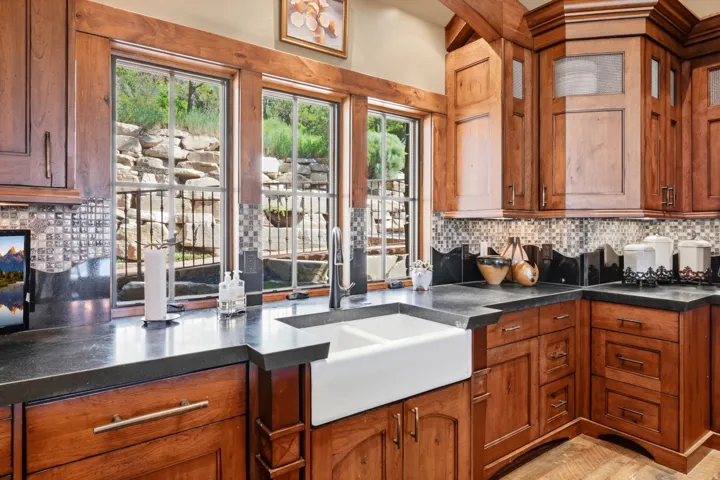 Kitchen featuring extensive wood cabinetry, dark countertops, a white farmhouse-style sink, and mosaic tile backsplash
