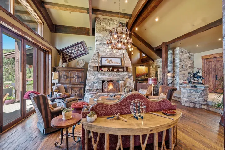 Spacious living area featuring a vaulted ceiling with exposed wood beams, a prominent stone fireplace, and wide plank wood-finish flooring