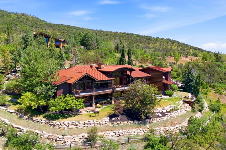 Multi-level residence featuring a rust-toned metal roof, exposed timber beams, and a wrap-around balcony