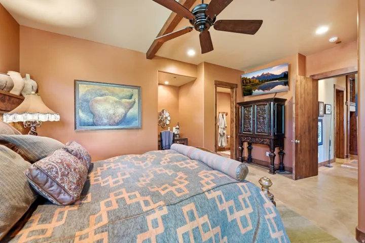 Spacious bedroom featuring warm-toned walls, wood-finish ceiling beams, and a ceiling fan