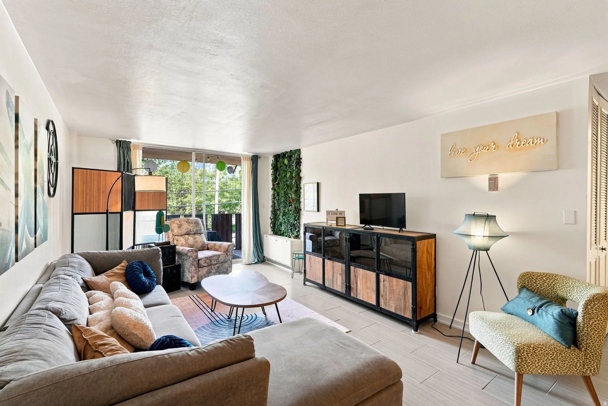 Bright, open living space featuring expansive glass sliding doors with natural light, light wood-finish flooring throughout, and a built-in media console with wood cabinetry and woven basket storage