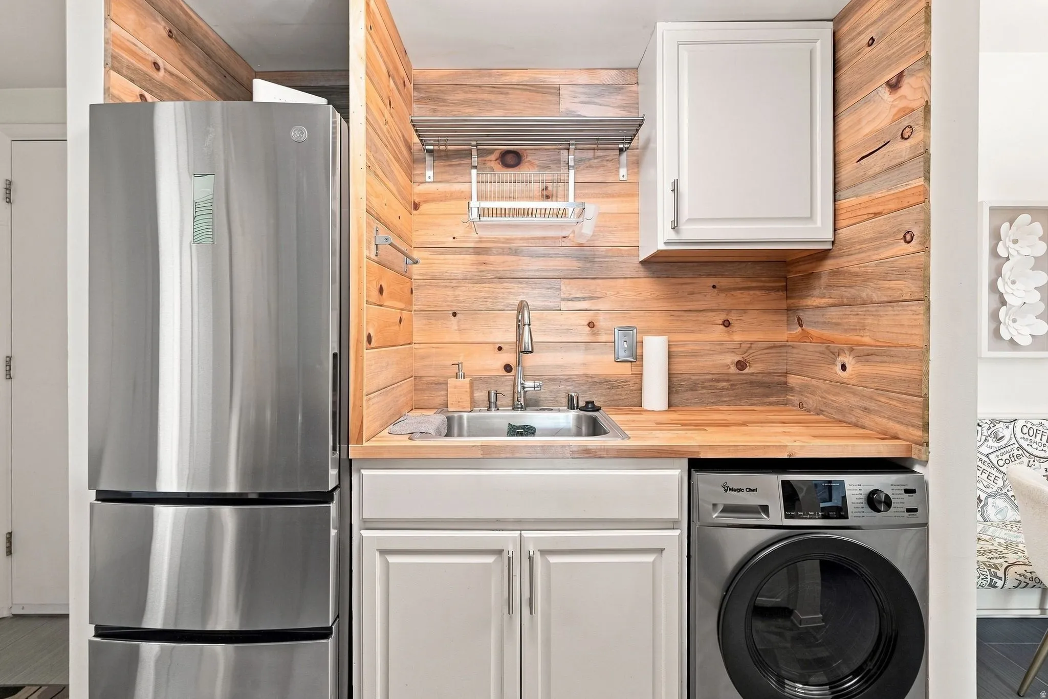 Stainless steel refrigerator, integrated washer, wood-finish countertop, stainless steel sink, and wood-finish paneling