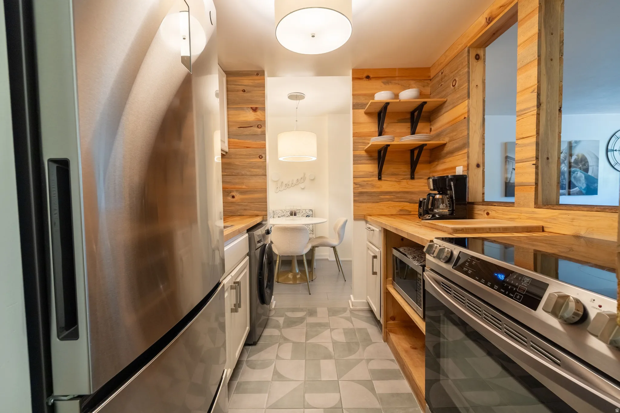 Galley kitchen featuring stainless steel appliances, wood-finish countertops, open shelving, and a wood-paneled accent wall