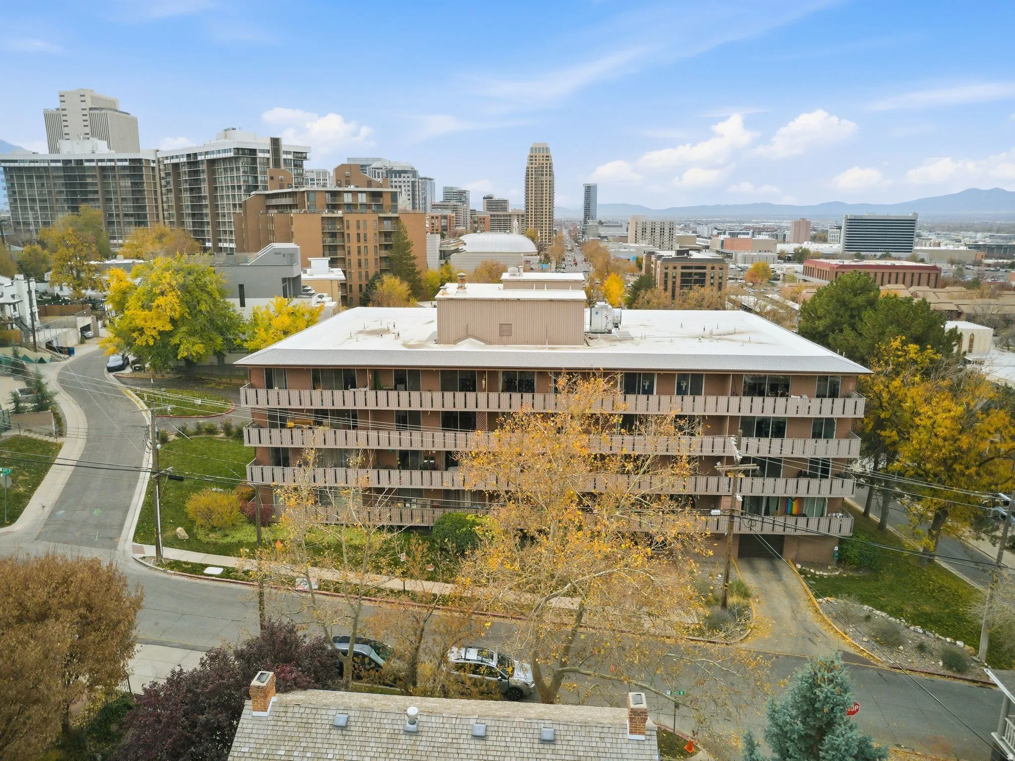 Multi-story building featuring exterior balconies, a flat roofline, surrounding mature trees, and a paved drive