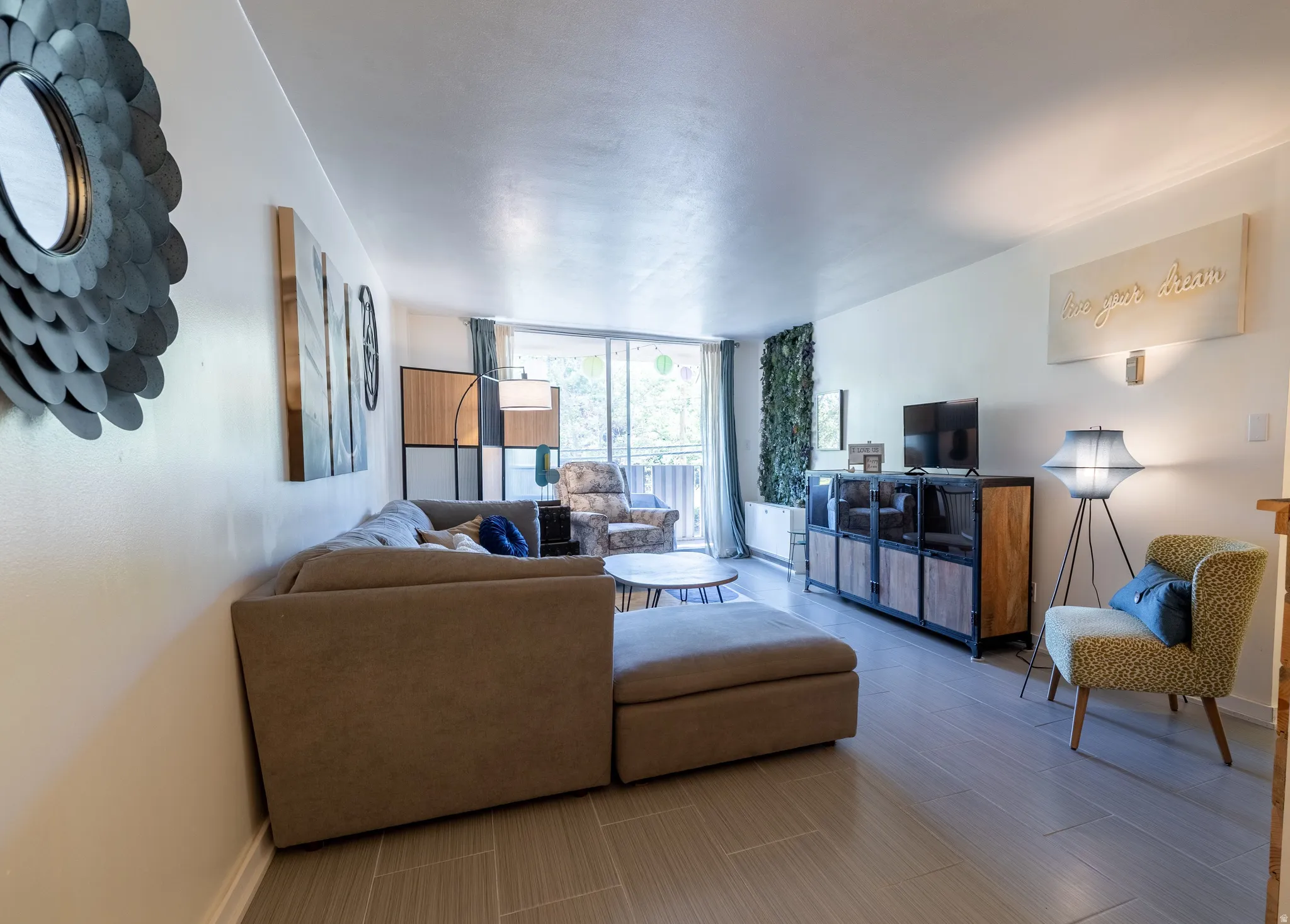 Spacious living area featuring light-toned tile flooring, white walls, and a large sliding glass door